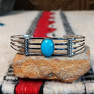 Silver cuff by Thomas Yazzie featuring a smooth oval blue turquoise stone centered within five slender silver bands and flanked by vertical beaded silver accents.