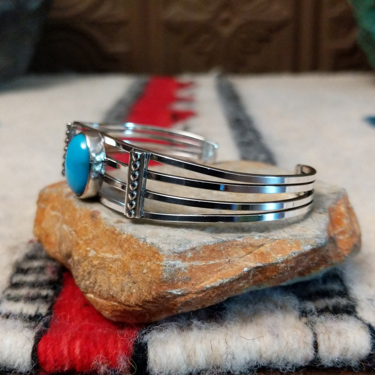 Silver cuff by Thomas Yazzie featuring a smooth oval blue turquoise stone centered within five slender silver bands and flanked by vertical beaded silver accents; side view.