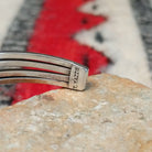 Silver cuff by Thomas Yazzie featuring a smooth oval blue turquoise stone centered within five slender silver bands and flanked by vertical beaded silver accents; artisan stamp.