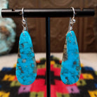 Turquoise Earrings by Ronald Chavez featuring elongated bright blue turquoise slabs with natural gray and brown matrix patterns, suspended from silver hooks.