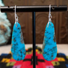 Turquoise Earrings by Ronald Chavez featuring elongated bright blue turquoise slabs with natural gray and brown matrix patterns, suspended from silver hooks; backside view.