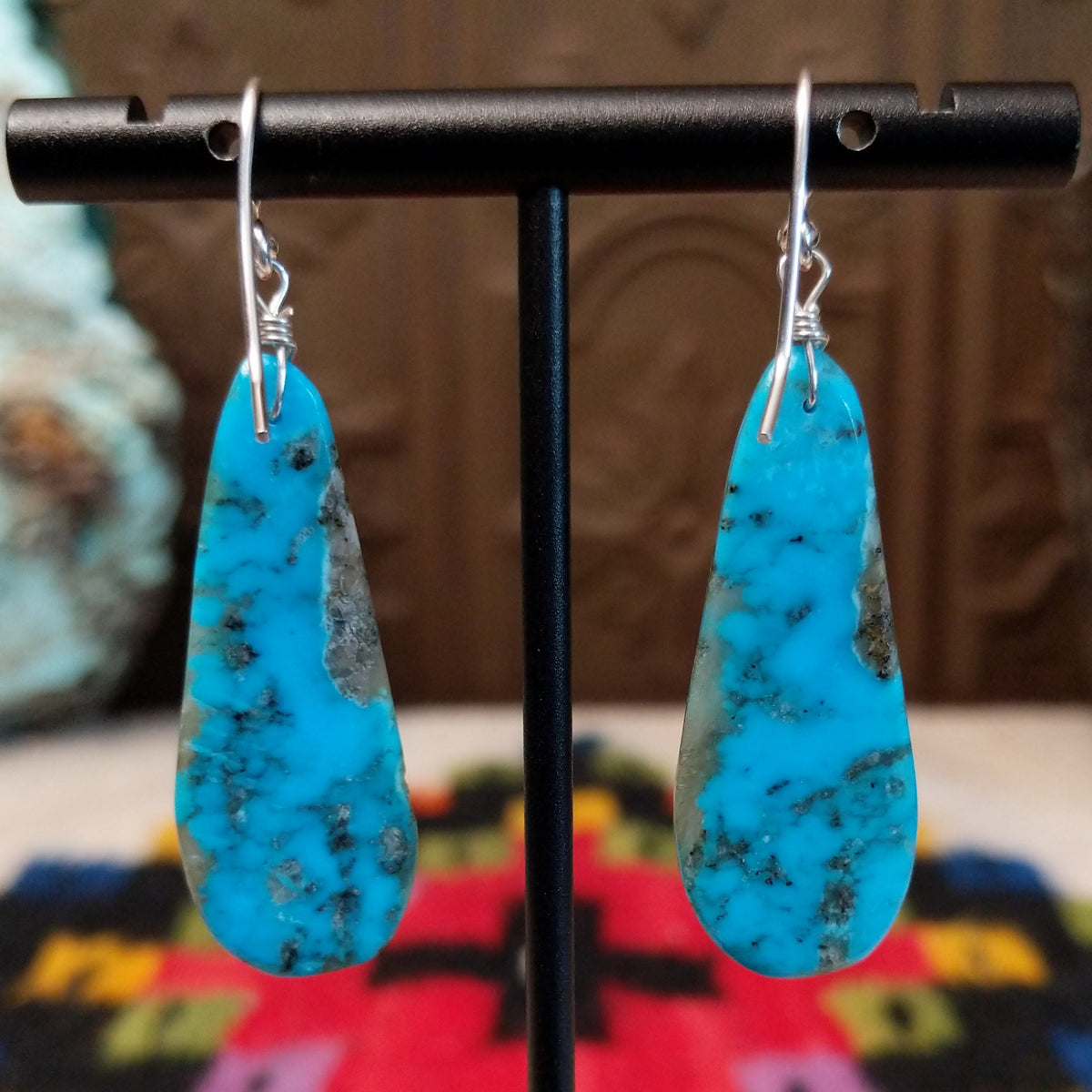 Turquoise Earrings by Ronald Chavez featuring elongated bright blue turquoise slabs with natural gray and brown matrix patterns, suspended from silver hooks; backside view.