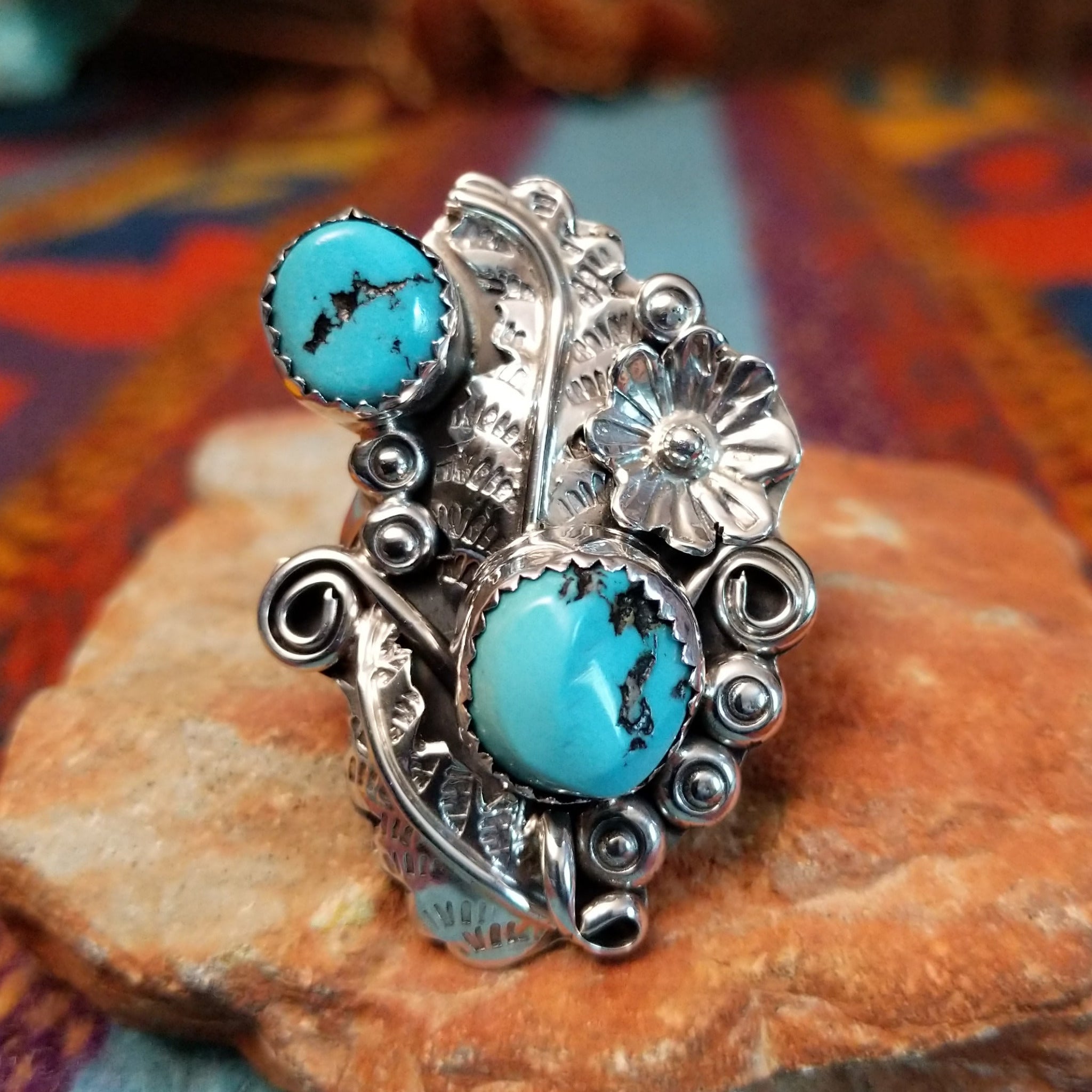 Turquoise Feather Ring by Harry B. Yazzie featuring two turquoise stones set in Sterling Silver with detailed feathers, a silver flower, scrollwork, and polished bead accents.