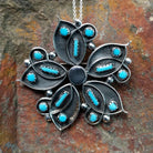 Handcrafted sterling silver turquoise flower pin and pendant by V. Booqua, featuring turquoise cabochons in a stylized floral design.