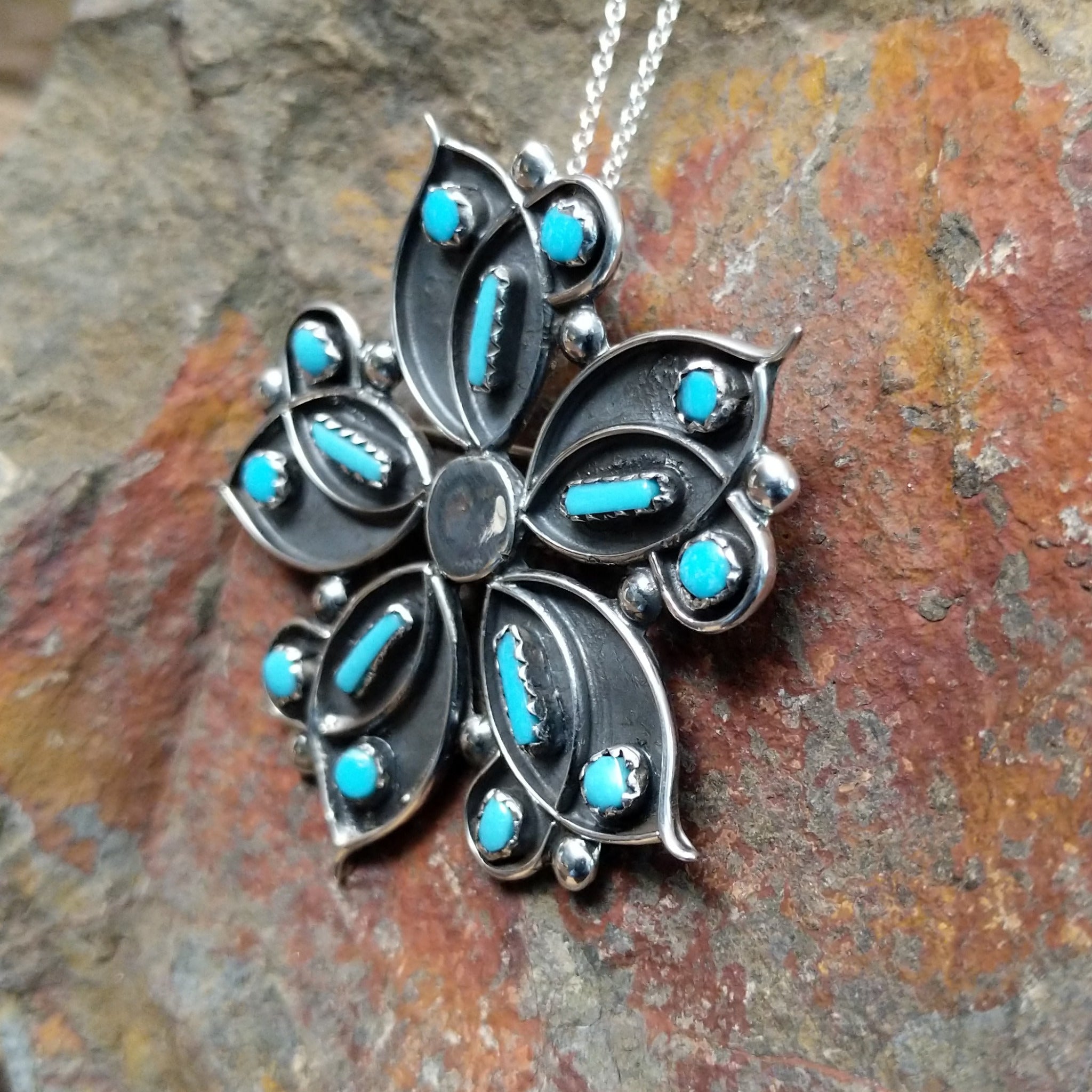 Handcrafted sterling silver turquoise flower pin and pendant by V. Booqua, featuring turquoise cabochons in a stylized floral design; side view.