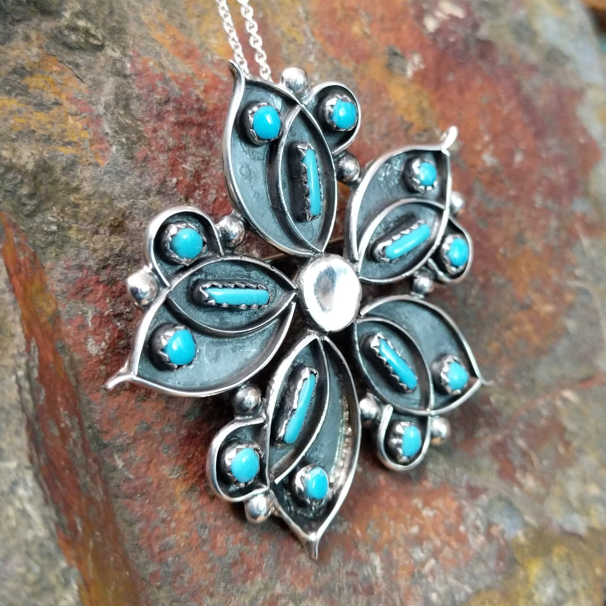 Handcrafted sterling silver turquoise flower pin and pendant by V. Booqua, featuring turquoise cabochons in a stylized floral design; side view.