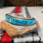 Silver cuff by Raymond Coriz featuring vibrant turquoise inlay with natural matrix and intricate geometric silver channel designs; side view.