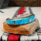 Silver cuff by Raymond Coriz featuring vibrant turquoise inlay with natural matrix and intricate geometric silver channel designs; side view.