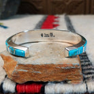 Silver cuff by Raymond Coriz featuring vibrant turquoise inlay with natural matrix and intricate geometric silver channel designs; underside view.