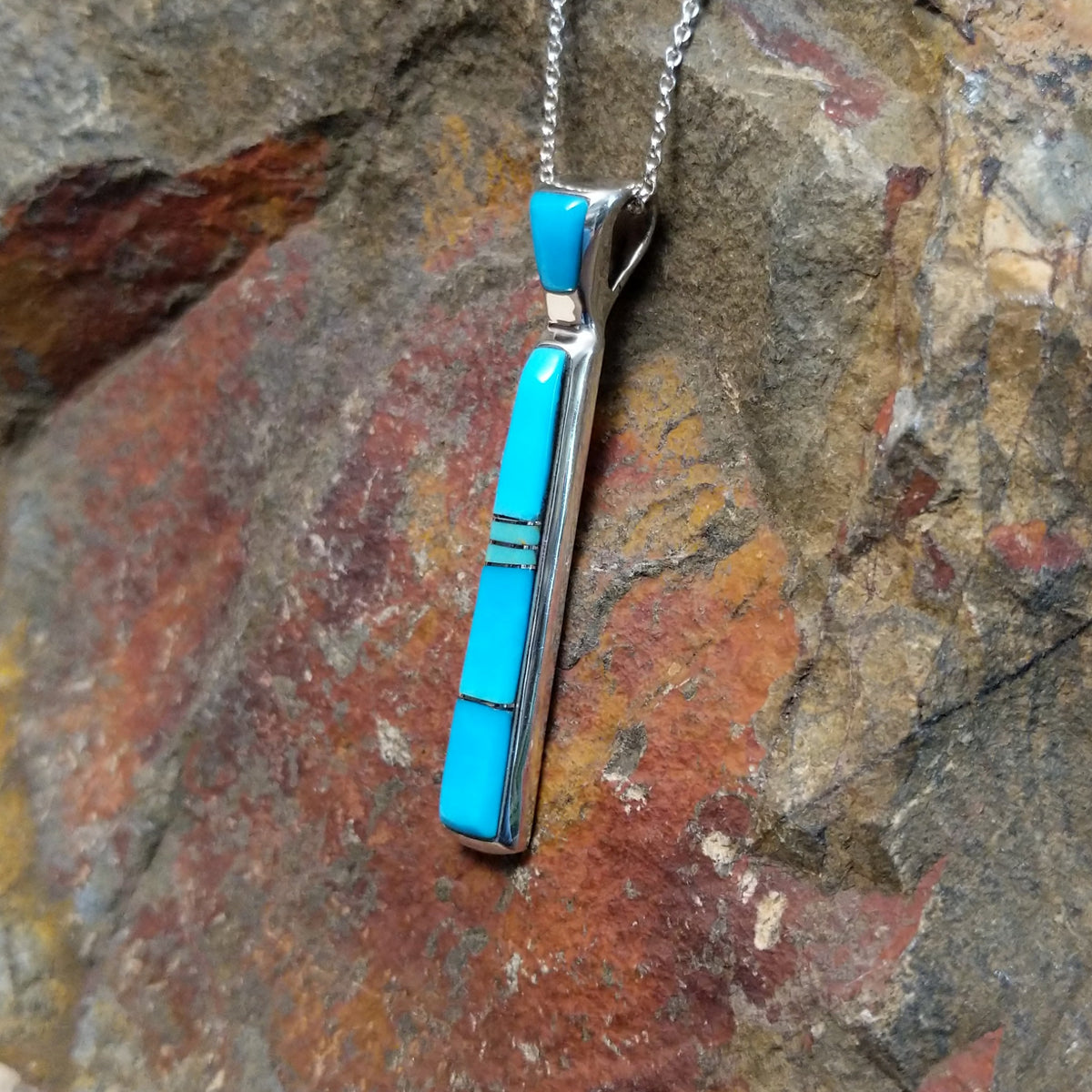 Turquoise inlay pendant by Stacy Spencer featuring an elongated geometric design with vibrant turquoise sections set in polished sterling silver and a turquoise-inlaid bail; side view.