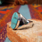 Turquoise Inlay Ring by Wilbert Grey featuring an elongated oval turquoise face with natural matrix, geometric silver channel inlay, and a polished tapered silver band; side view.