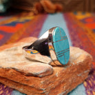Turquoise Inlay Ring by Wilbert Grey featuring an elongated oval turquoise face with natural matrix, geometric silver channel inlay, and a polished tapered silver band; side view.