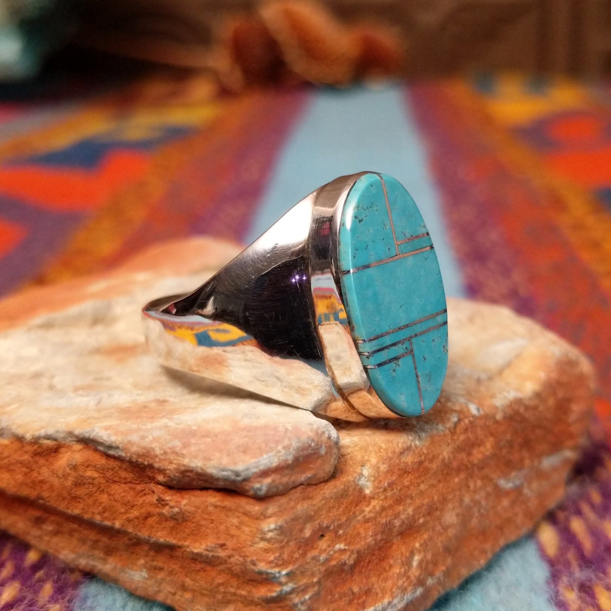 Turquoise Inlay Ring by Wilbert Grey featuring an elongated oval turquoise face with natural matrix, geometric silver channel inlay, and a polished tapered silver band; side view.