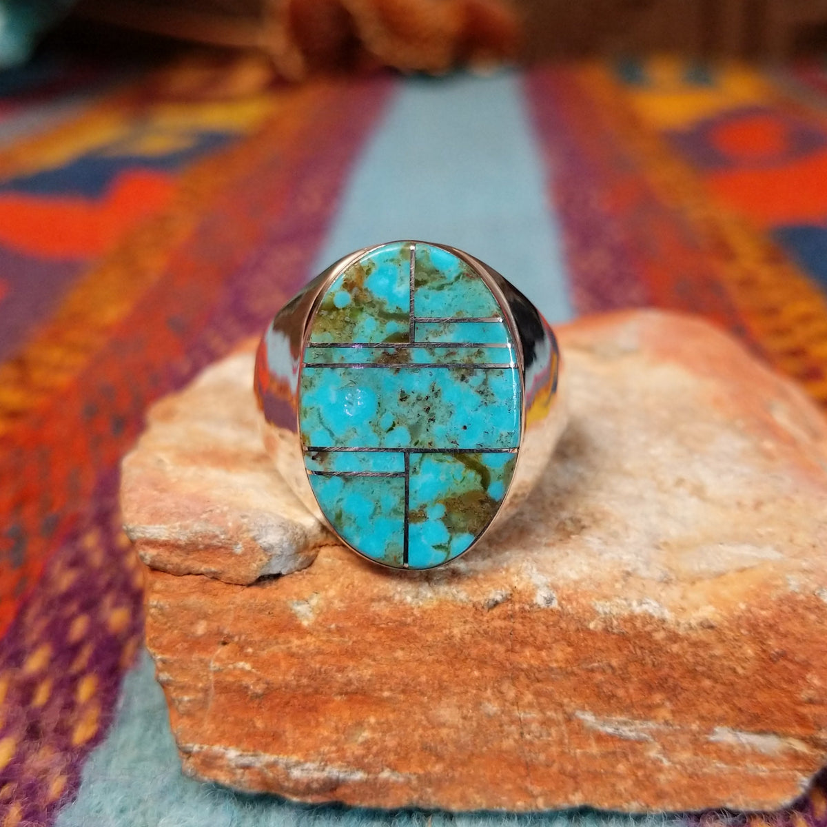 Turquoise Inlay Ring by Wilbert Grey featuring an oval turquoise face with natural brown and green matrix, divided by geometric silver channels and set in a wide polished silver band.