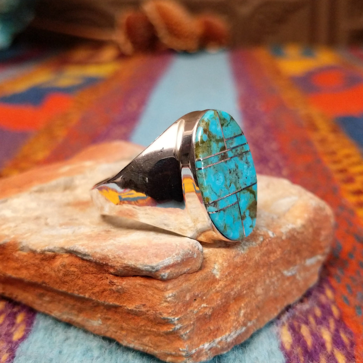 Turquoise Inlay Ring by Wilbert Grey featuring an oval turquoise face with natural brown and green matrix, divided by geometric silver channels and set in a wide polished silver band; side view.