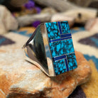 Sterling silver Navajo rectangle ring by Wilbert Grey featuring natural turquoise with black matrix and lapis lazuli geometric inlay in a polished signet-style setting; side view.