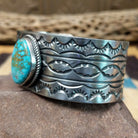 Turquoise Mountain turquoise cuff by E. Piaso, featuring a blue turquoise stone with a natural brown matrix set in a handcrafted wide sterling silver cuff; side view.