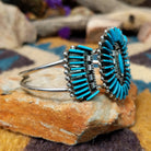 Handcrafted sterling silver cuff by Barton Cooeyate featuring a turquoise needlepoint concho centerpiece with matching side conchos, twisted rope detailing, silver bead accents, and a triple-shank cuff; side view.