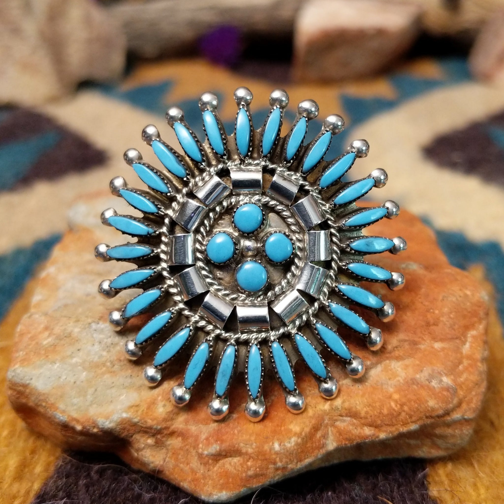 Handcrafted sterling silver Zuni concho ring featuring a turquoise needlepoint sunburst design with marquise-cut turquoise stones surrounding a central cluster of round turquoise cabochons, accented by polished silver details and twisted rope borders.