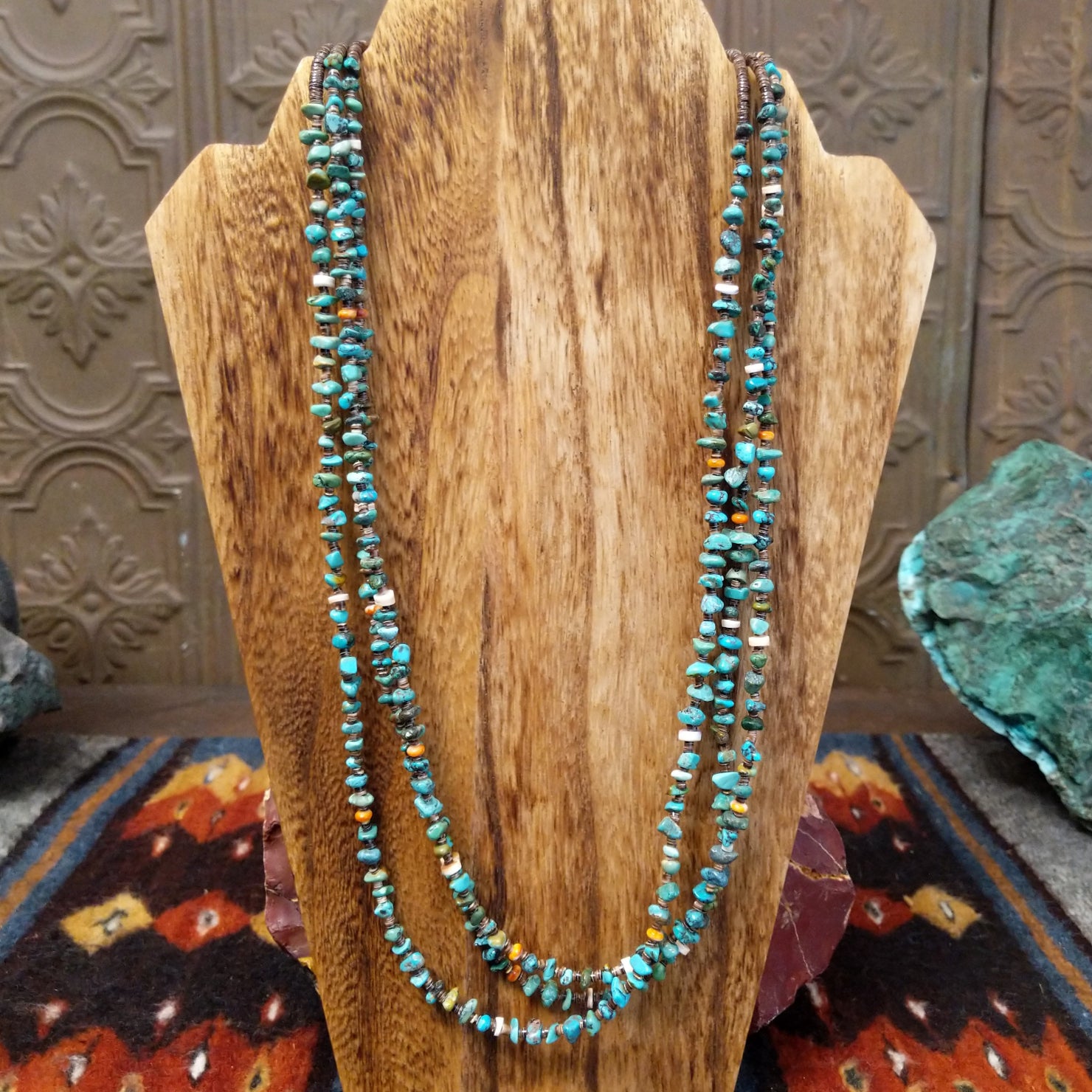 A multi-strand necklace featuring turquoise and orange spiny oyster shell heishi beads, accented with brown pen shell at the sterling silver clasp.