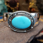Silver cuff featuring an oval turquoise stone set in an intricate layered silver setting.
