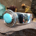 Silver cuff featuring an oval turquoise stone set in an intricate layered silver setting.