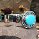 Silver cuff featuring an oval turquoise stone set in an intricate layered silver setting.