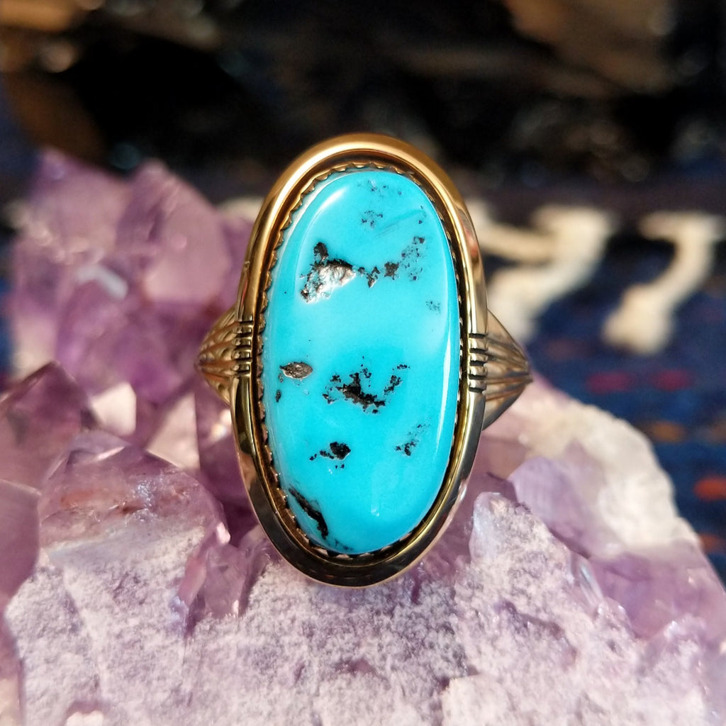 A gold ring with an oval turquoise stone featuring black matrix.
