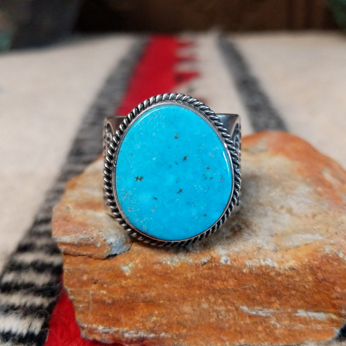 Turquoise ring by Burt Francisco featuring a large oval bright blue turquoise stone with subtle matrix, framed by twisted silver rope detailing on a wide silver band.