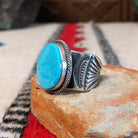 Turquoise ring by Burt Francisco featuring a large oval bright blue turquoise stone with subtle matrix, framed by twisted silver rope detailing on a wide silver band; side view.