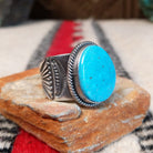 Turquoise ring by Burt Francisco featuring a large oval bright blue turquoise stone with subtle matrix, framed by twisted silver rope detailing on a wide silver band; side view.