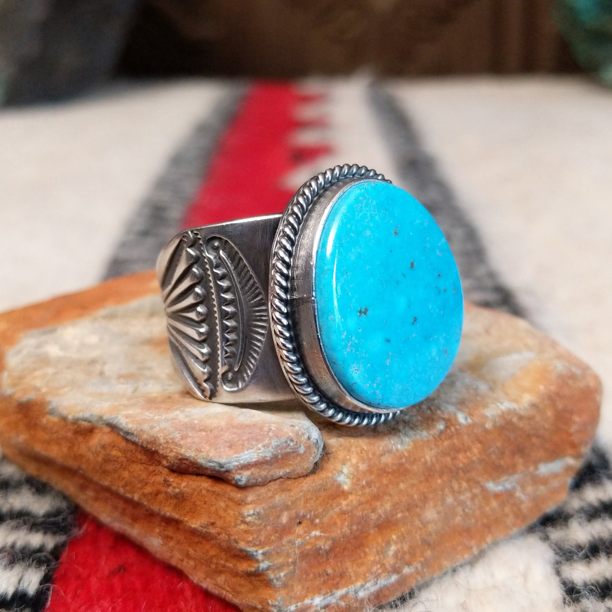 Turquoise ring by Burt Francisco featuring a large oval bright blue turquoise stone with subtle matrix, framed by twisted silver rope detailing on a wide silver band; side view.