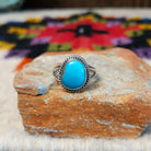 This Turquoise Ring by Byron Begay features a bright blue oval turquoise stone set in sterling silver with a twisted rope border and split-shank band.
