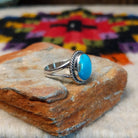 This Turquoise Ring by Byron Begay features a bright blue oval turquoise stone set in sterling silver with a twisted rope border and split-shank band; side view.