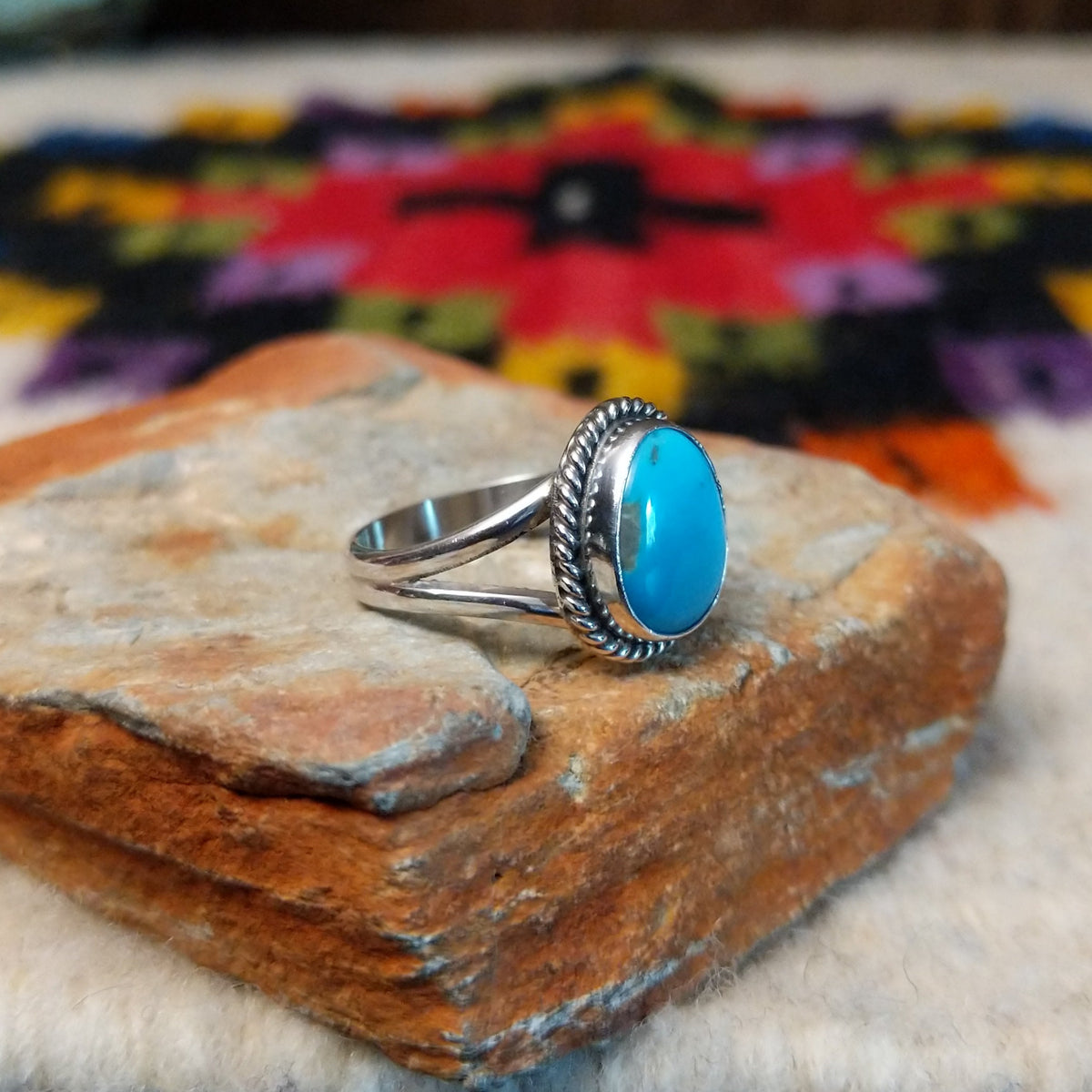 This Turquoise Ring by Byron Begay features a bright blue oval turquoise stone set in sterling silver with a twisted rope border and split-shank band; side view.