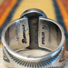 Turquoise Ring by Lowell Draper & Bernyse Chavez featuring a large oval turquoise stone with natural matrix, a polished silver bezel, and a wide silver band decorated with stamped sunburst patterns and geometric detailing; artisan and Sterling Silver stamp.