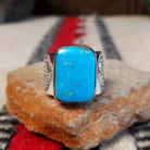 Turquoise ring by Lucy Jake featuring a large rectangular bright blue turquoise stone with subtle natural matrix, set in a wide silver band with stamped detailing.