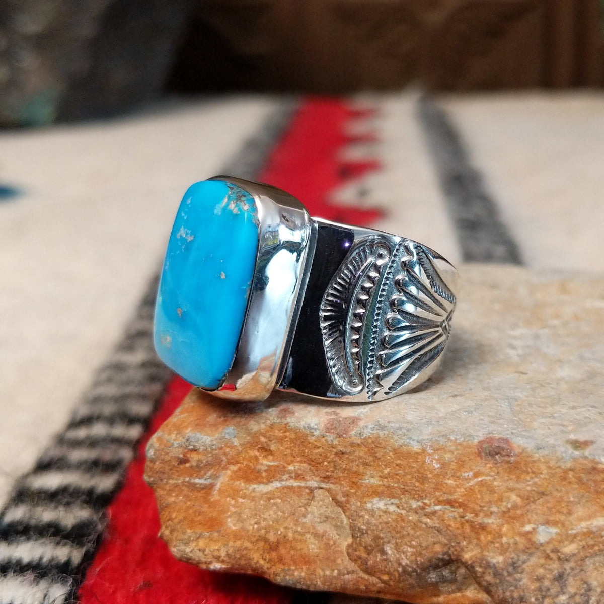 Turquoise ring by Lucy Jake featuring a large rectangular bright blue turquoise stone with subtle natural matrix, set in a wide silver band with stamped detailing; side view.