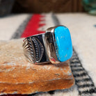 Turquoise ring by Lucy Jake featuring a large rectangular bright blue turquoise stone with subtle natural matrix, set in a wide silver band with stamped detailing; side view.