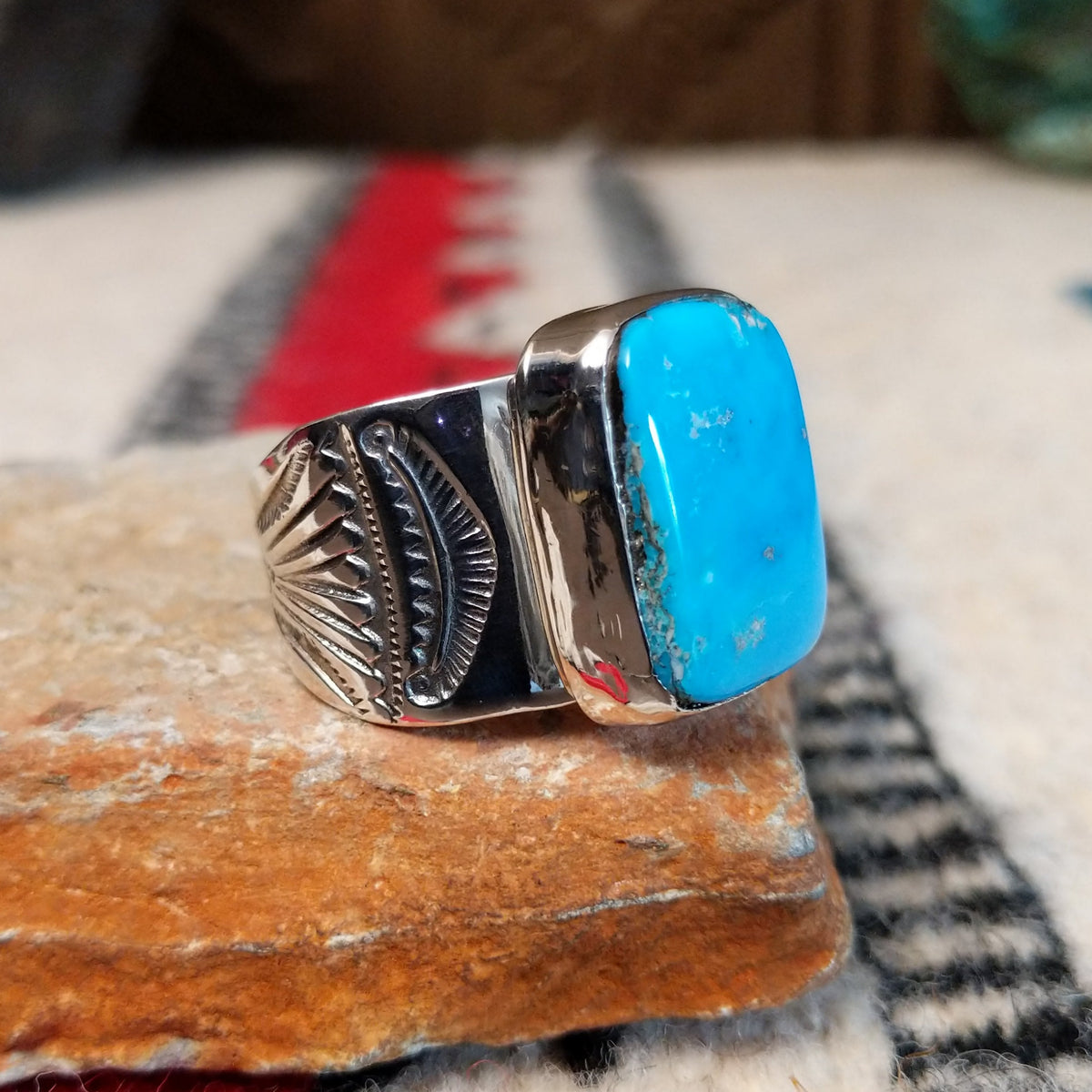 Turquoise ring by Lucy Jake featuring a large rectangular bright blue turquoise stone with subtle natural matrix, set in a wide silver band with stamped detailing; side view.