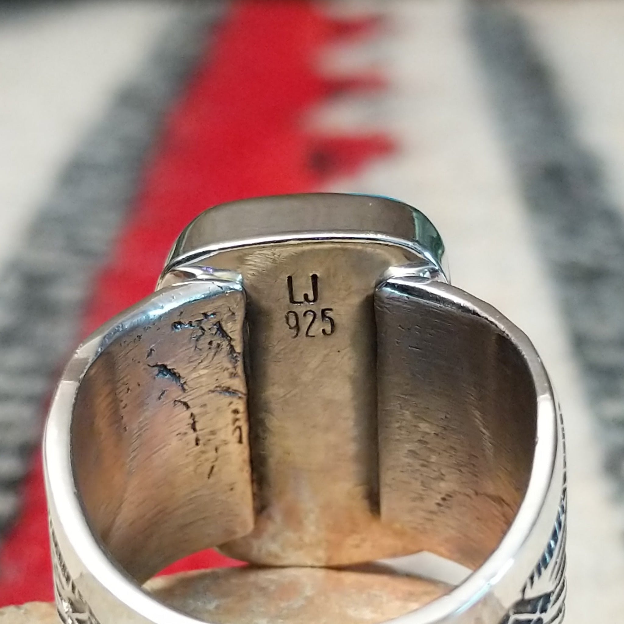 Turquoise ring by Lucy Jake featuring a large rectangular bright blue turquoise stone with subtle natural matrix, set in a wide silver band with stamped detailing; artisan and .925 (Sterling Silver) stamp.