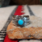 Turquoise ring by Raymond Coriz featuring a round turquoise stone centered in a wide silver band with detailed stamped, radiating, and curved designs.