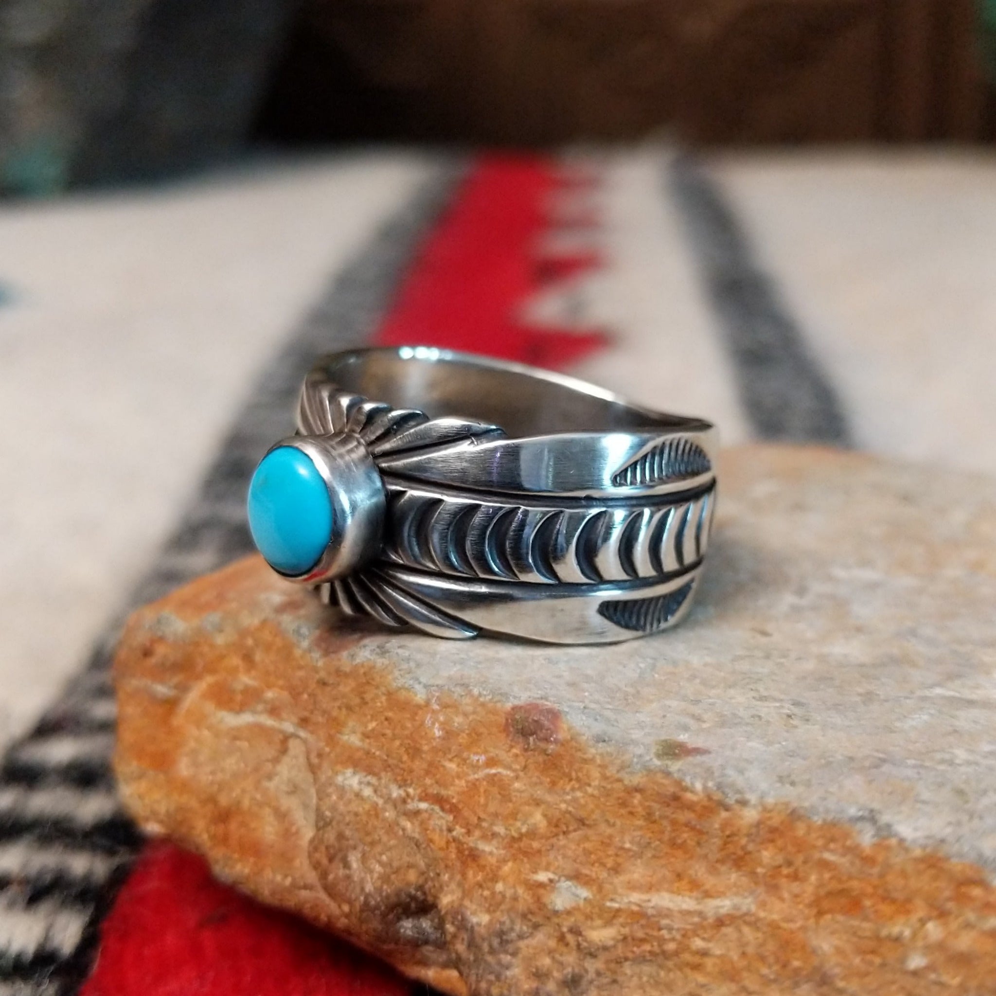 Turquoise ring by Raymond Coriz featuring a round turquoise stone centered in a wide silver band with detailed stamped, radiating, and curved designs; side view.