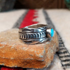 Turquoise ring by Raymond Coriz featuring a round turquoise stone centered in a wide silver band with detailed stamped, radiating, and curved designs; side view.