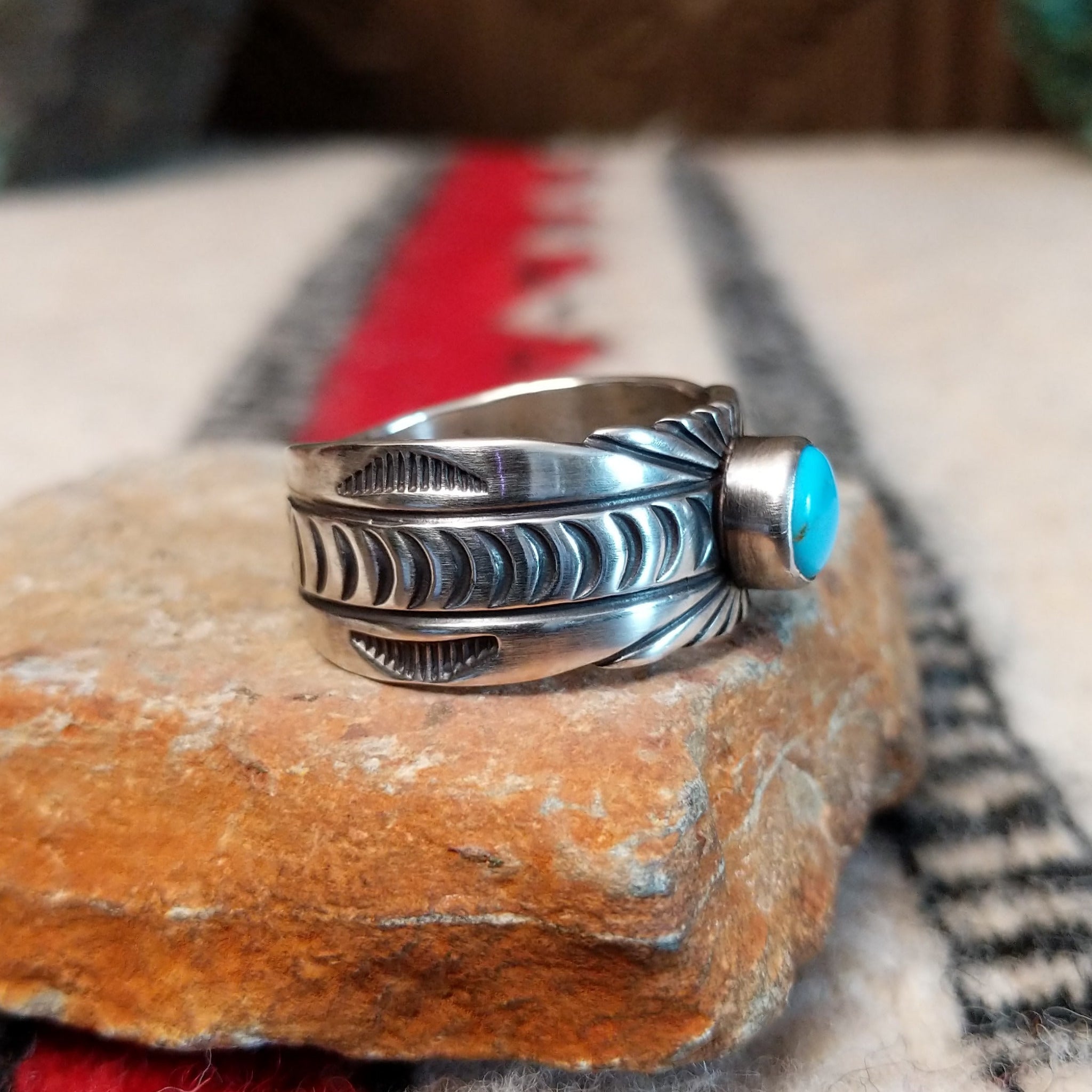 Turquoise ring by Raymond Coriz featuring a round turquoise stone centered in a wide silver band with detailed stamped, radiating, and curved designs; side view.