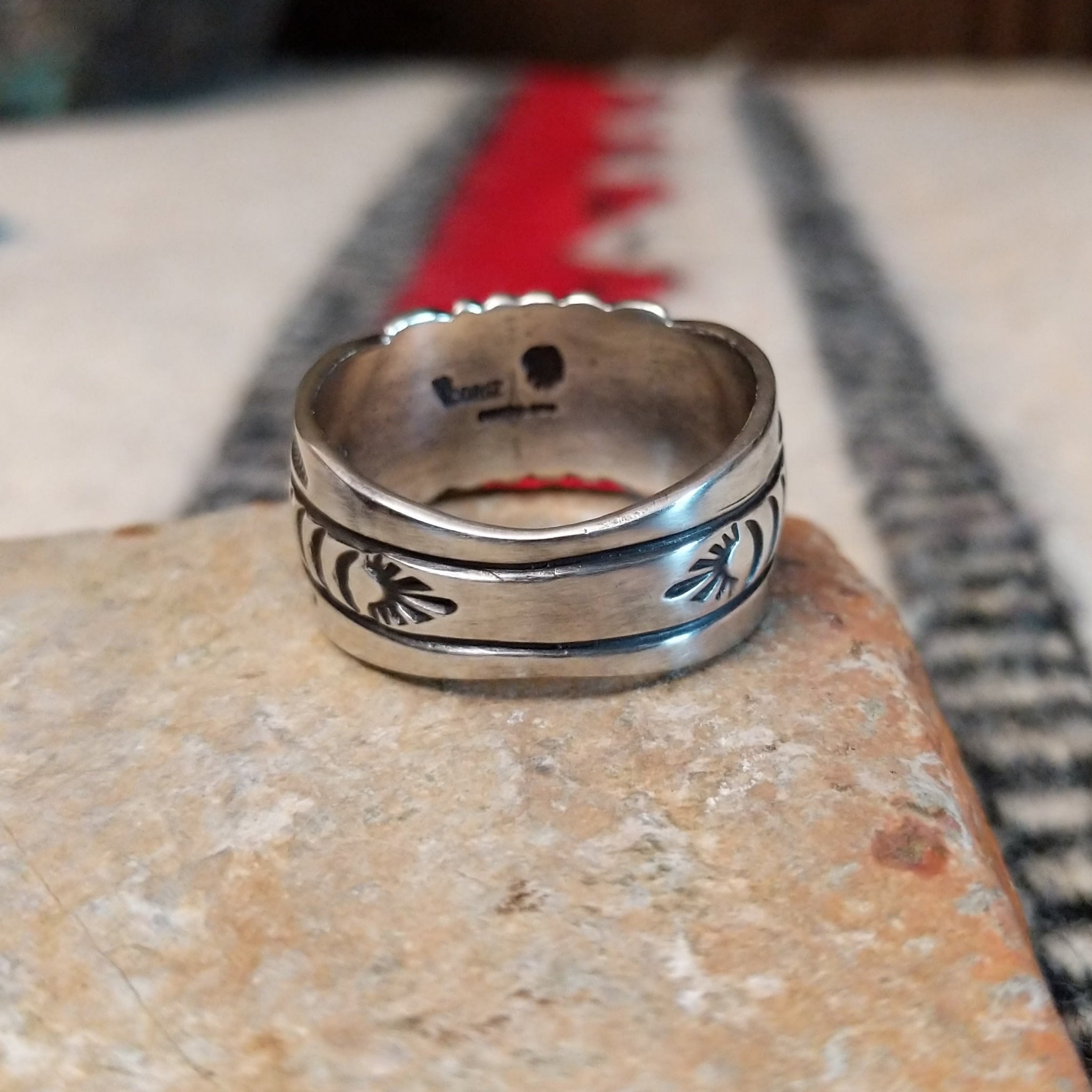 Turquoise ring by Raymond Coriz featuring a round turquoise stone centered in a wide silver band with detailed stamped, radiating, and curved designs; underside view.
