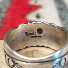 Turquoise ring by Raymond Coriz featuring a round turquoise stone centered in a wide silver band with detailed stamped, radiating, and curved designs; artisan and Sterling Silver stamp.