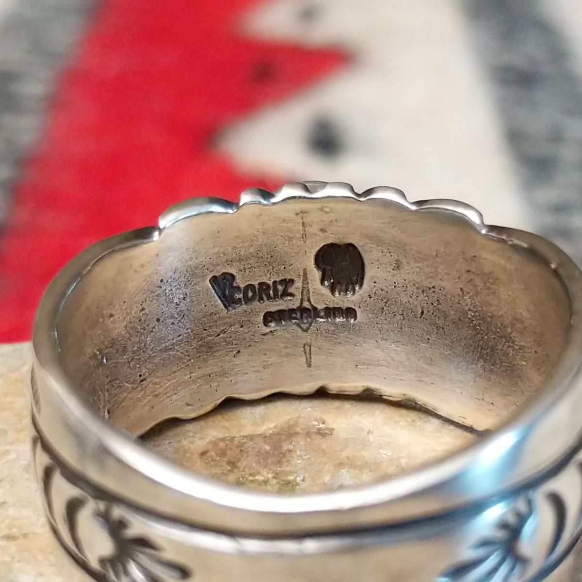 Turquoise ring by Raymond Coriz featuring a round turquoise stone centered in a wide silver band with detailed stamped, radiating, and curved designs; artisan and Sterling Silver stamp.
