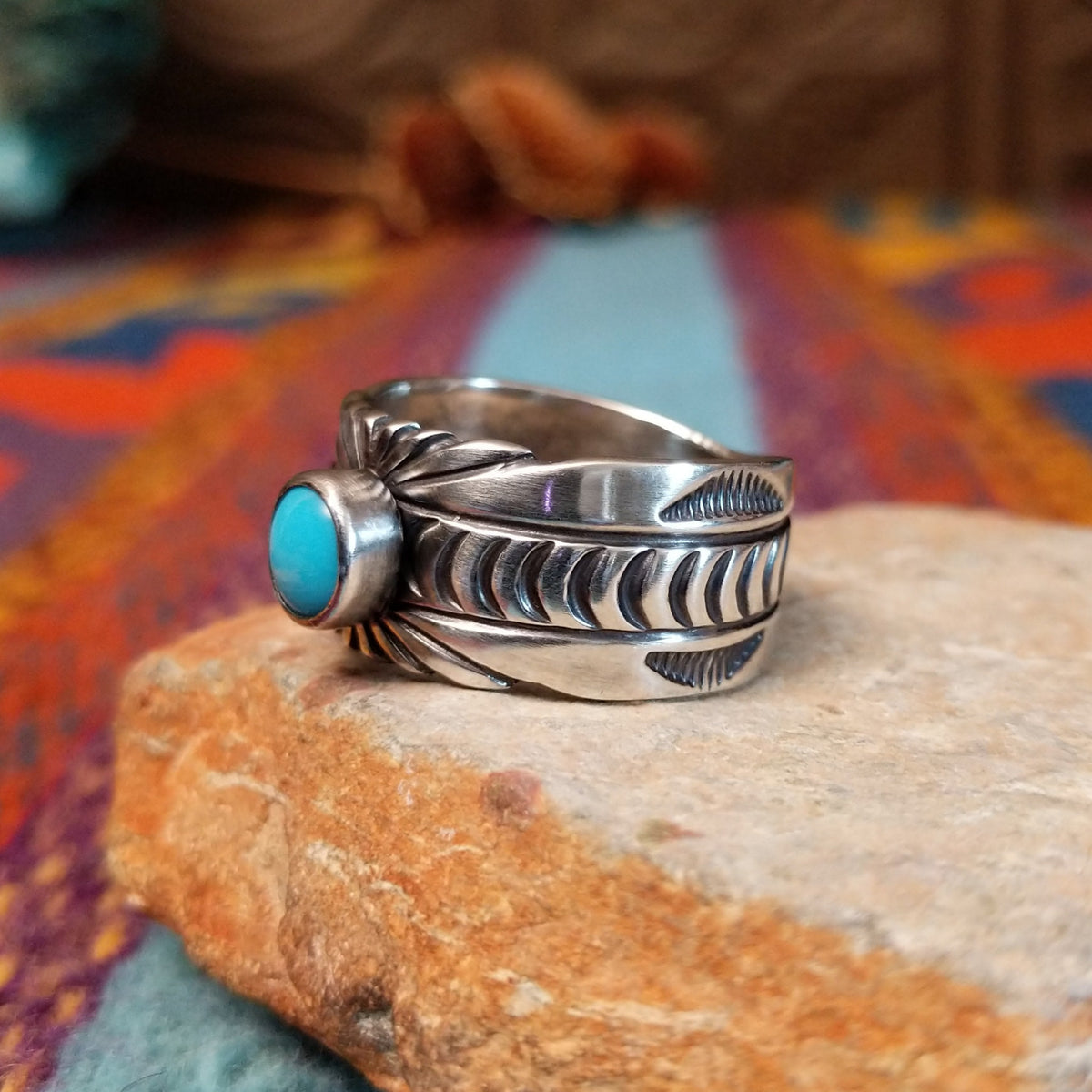 Turquoise Ring by Raymond Coriz featuring a round bright-blue turquoise cabochon centered on a wide silver band with hand-stamped curved and sunburst designs; side view.