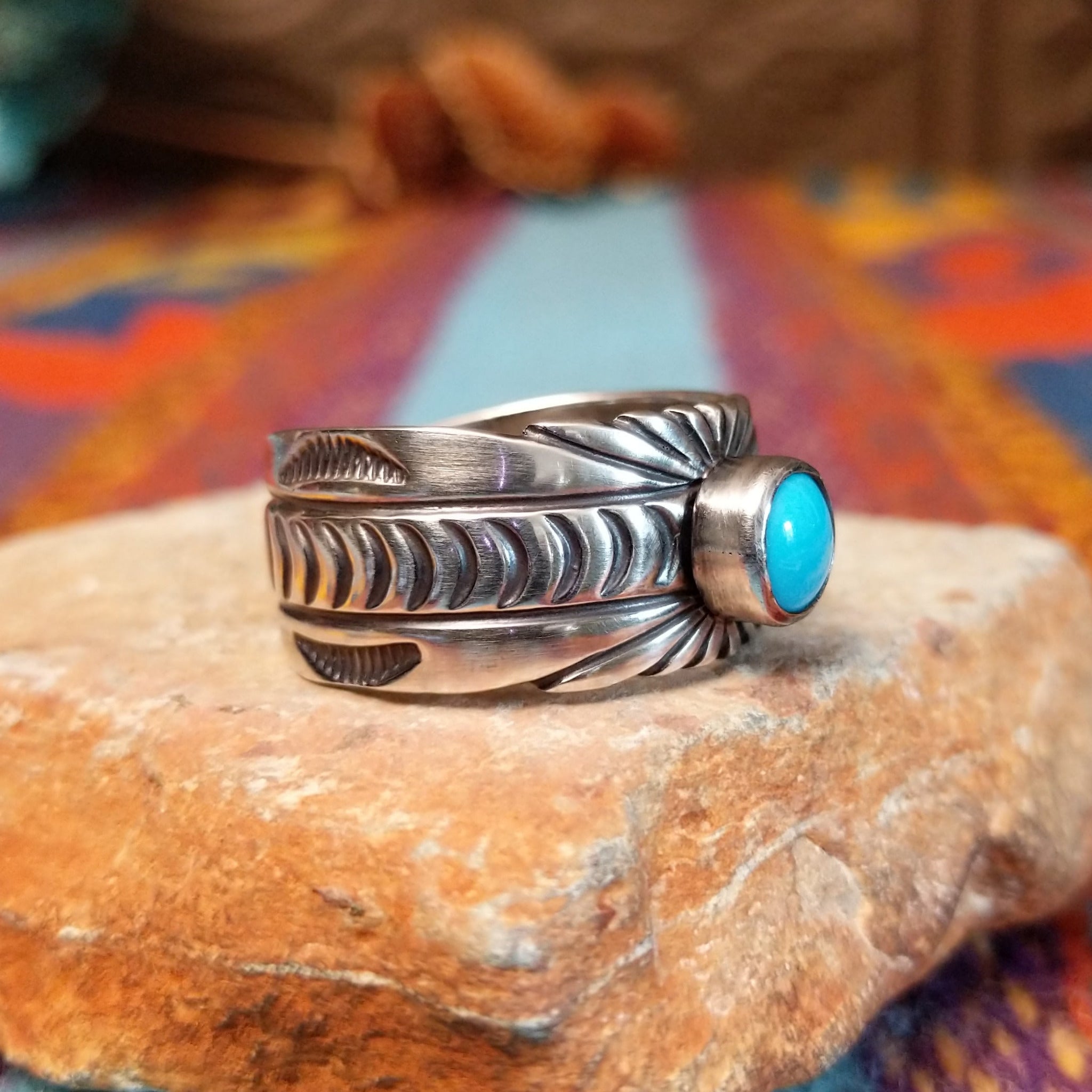 Turquoise Ring by Raymond Coriz featuring a round bright-blue turquoise cabochon centered on a wide silver band with hand-stamped curved and sunburst designs; side view.